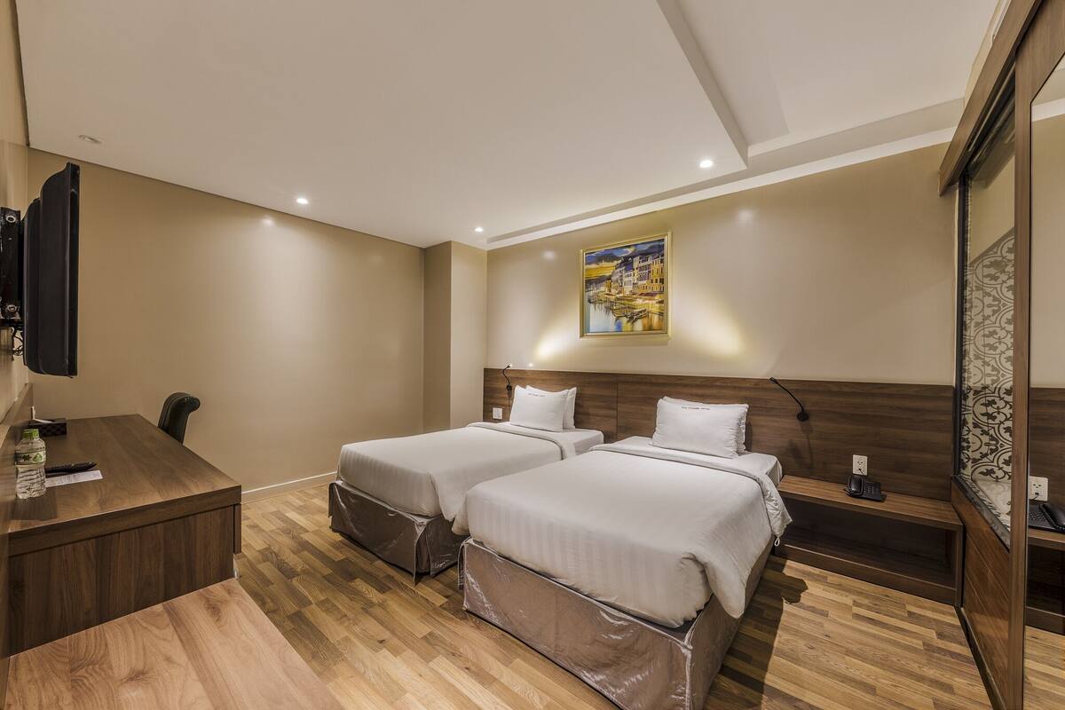 A hotel room with two beds, a wooden desk, a telephone, and a painting on the wall.