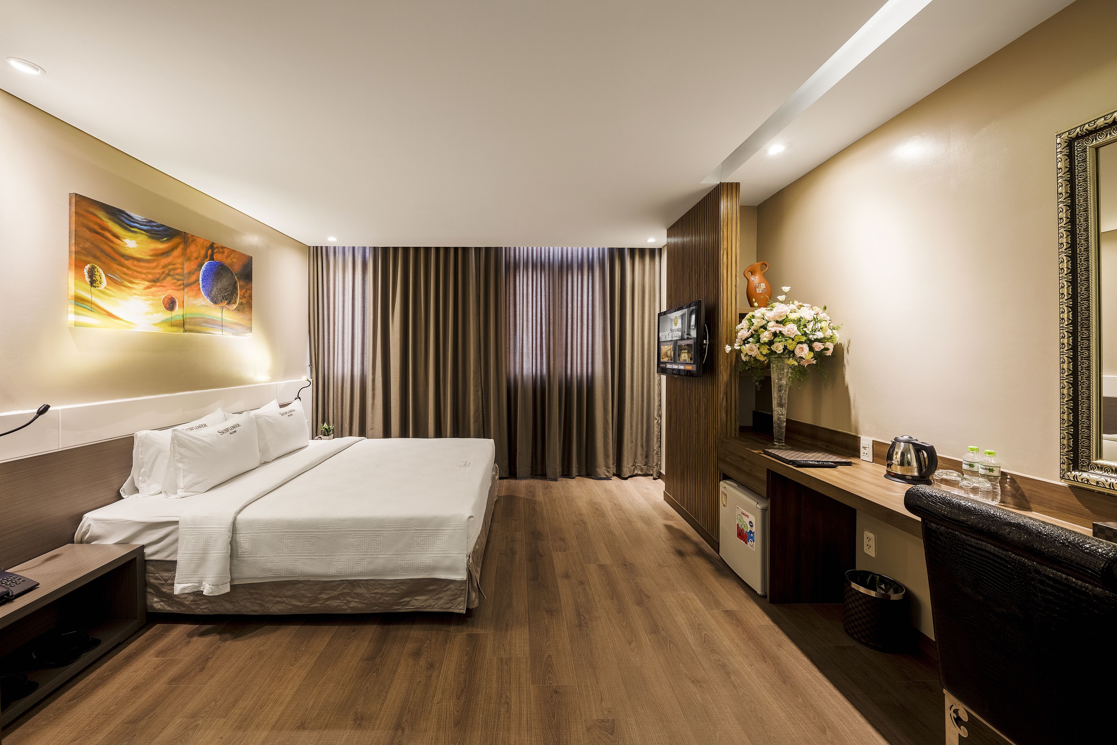 A hotel room with a bed, a desk, a TV, a mirror, and a window with curtains.