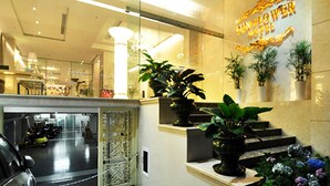 Un vestíbulo de hotel con mostrador de recepción, plantas en macetas y una escalera que conduce al piso superior.
