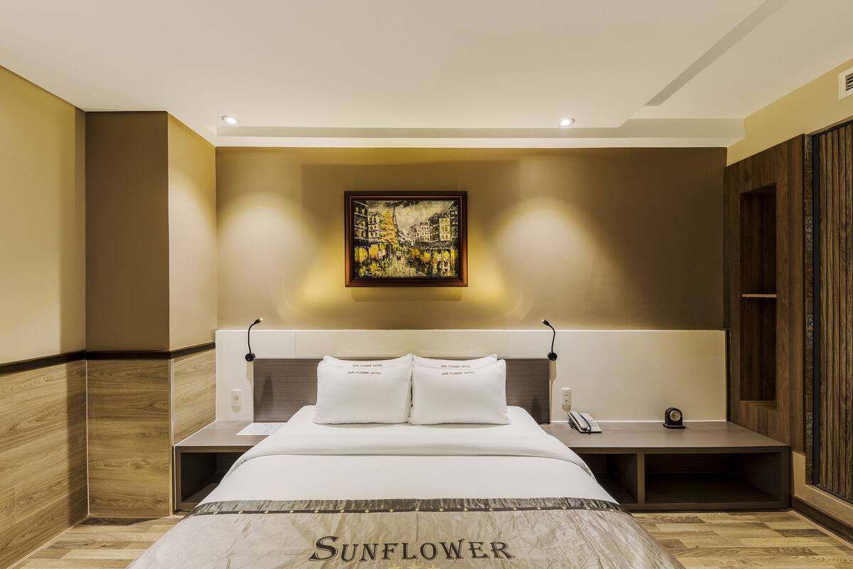 A hotel room with a bed, a nightstand, a wall-mounted painting, and a wooden wardrobe.