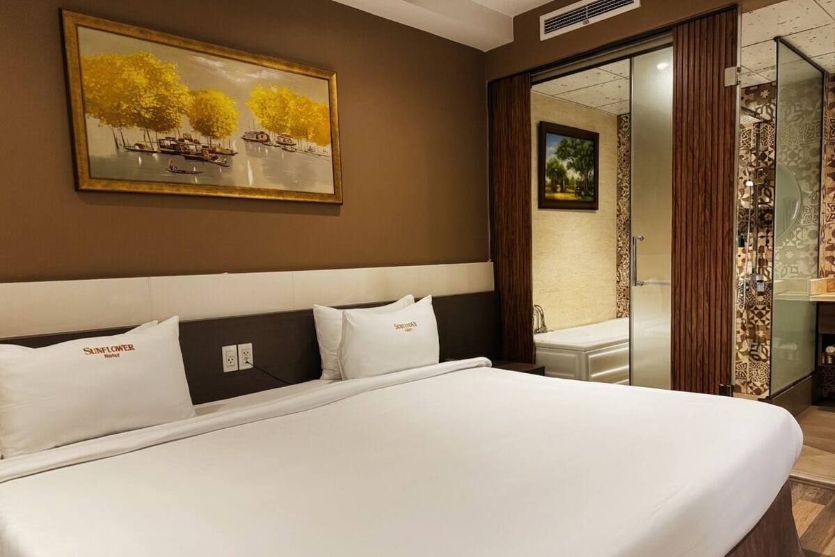 A hotel room with a large bed, a painting on the wall, and a sliding door leading to a bathroom.