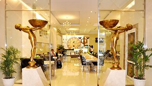 Un moderno vestíbulo de hotel con un mostrador de recepción central, zona de estar y esculturas doradas decorativas.