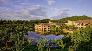 A resort with multiple buildings, a central structure reflecting in a lake, surrounded by dense greenery and hills in the background. - NARADA Resort & Spa Liangzhu (Hangzhou)