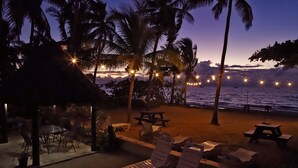 Une terrasse au bord de la plage, avec des chaises longues, des tables et des guirlandes lumineuses.