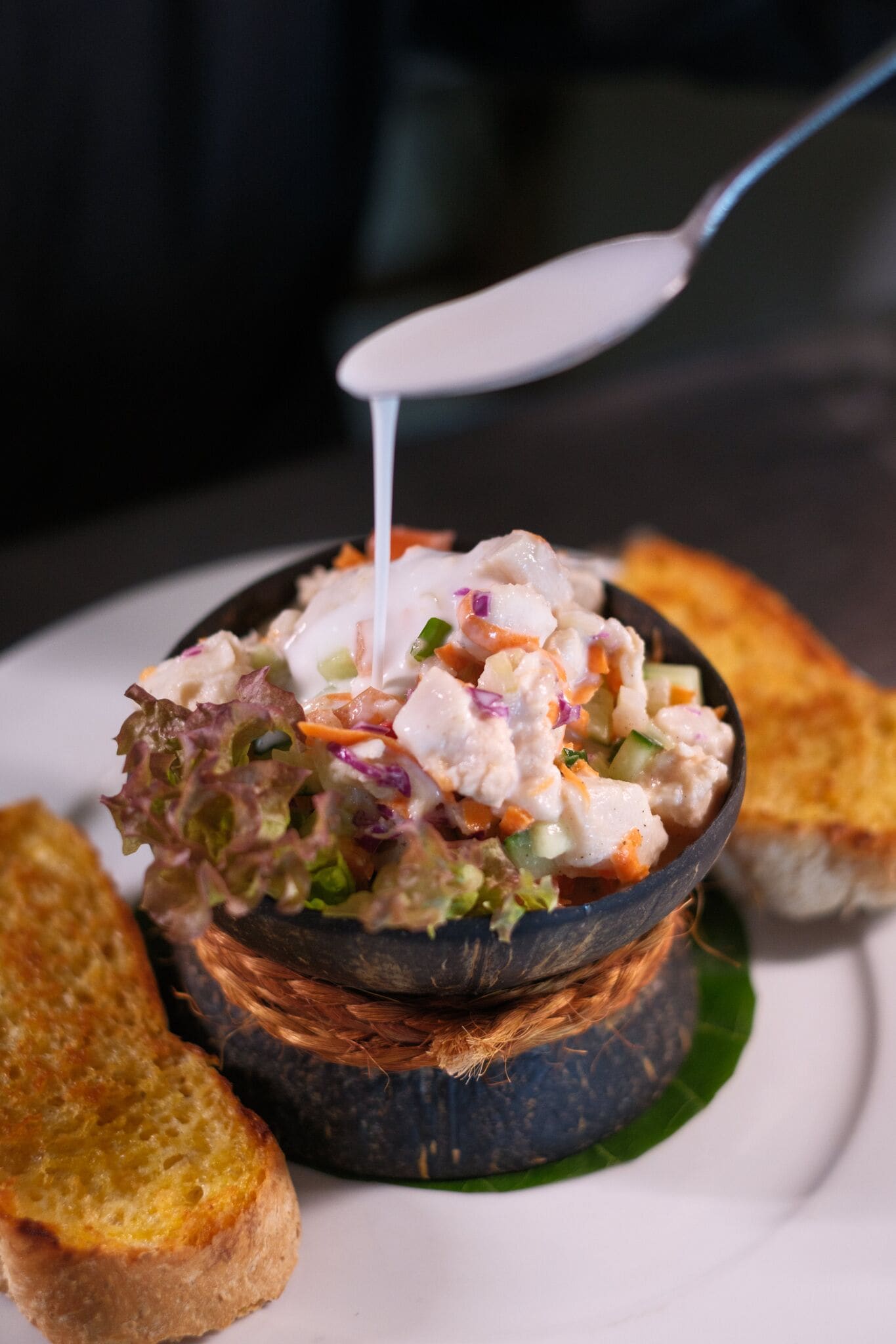 Un bol de salade de fruits de mer, accompagné d’une cuillère, servi avec des tranches de pain grillé sur une assiette.