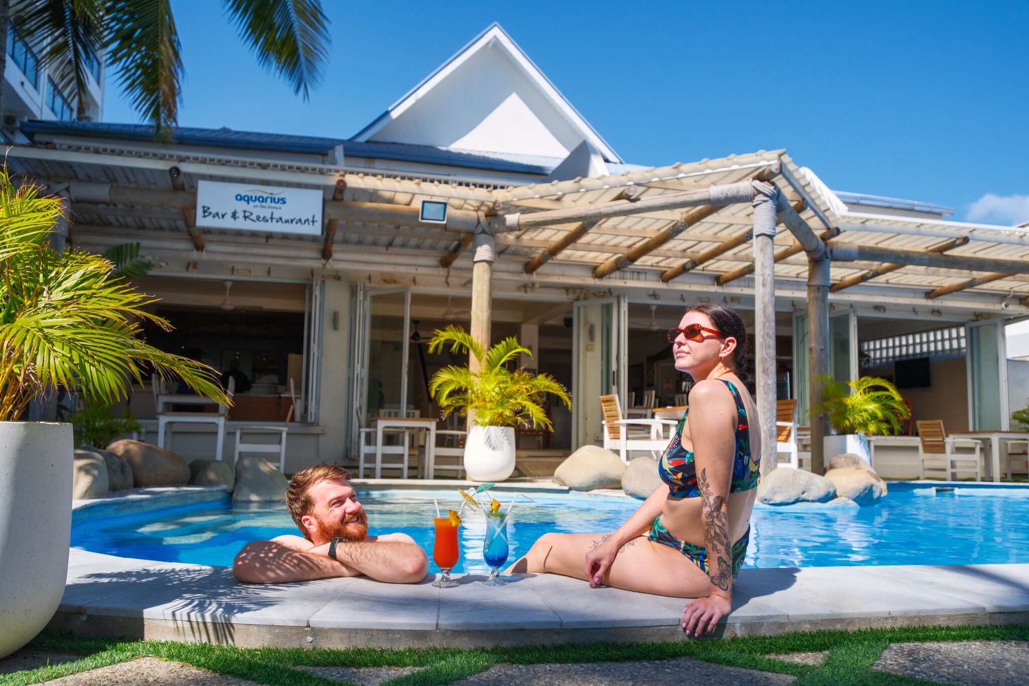 Uma área à beira da piscina com um bar e restaurante chamados 'Aquarius Bar & Restaurant' ao fundo.