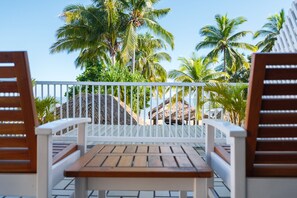 A wooden table and two wooden chairs on a balcony with a white railing, overlooking palm trees and a beach. - Aquarius on the Beach (Nadi)
