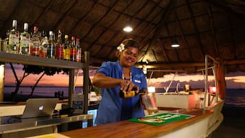 A bar area with a view of the sunset over the ocean, a laptop on the counter, and various bottles of alcohol.