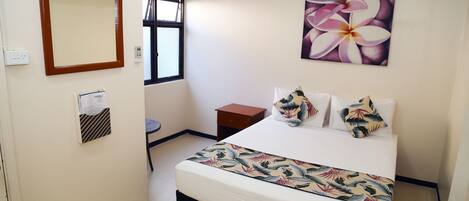 Habitación de hotel con una cama, una mesita de noche, un espejo, una ventana y aire acondicionado instalado en la pared.