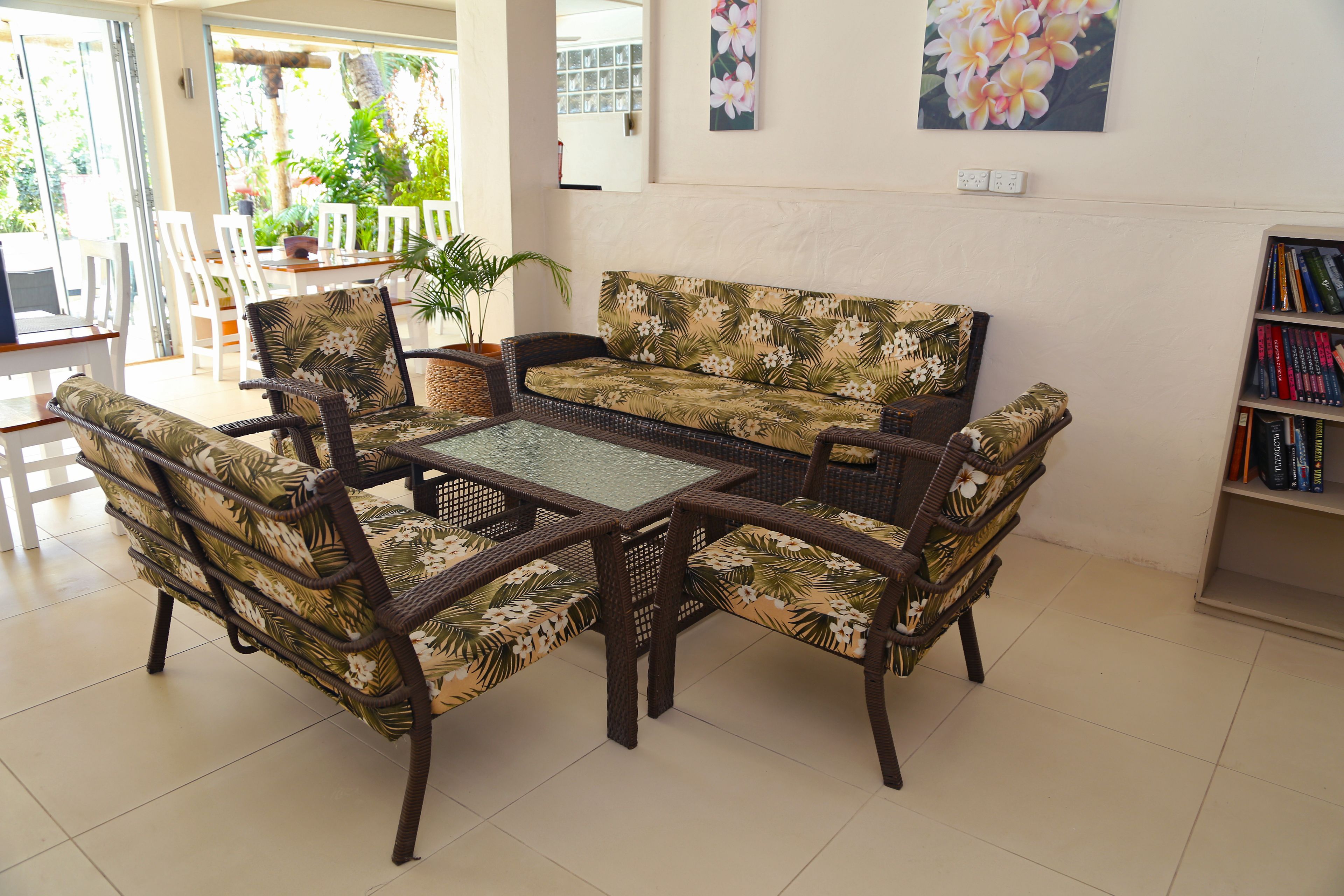 A living room with a sofa, chairs, and a coffee table. There is a bookshelf with books and a potted plant.