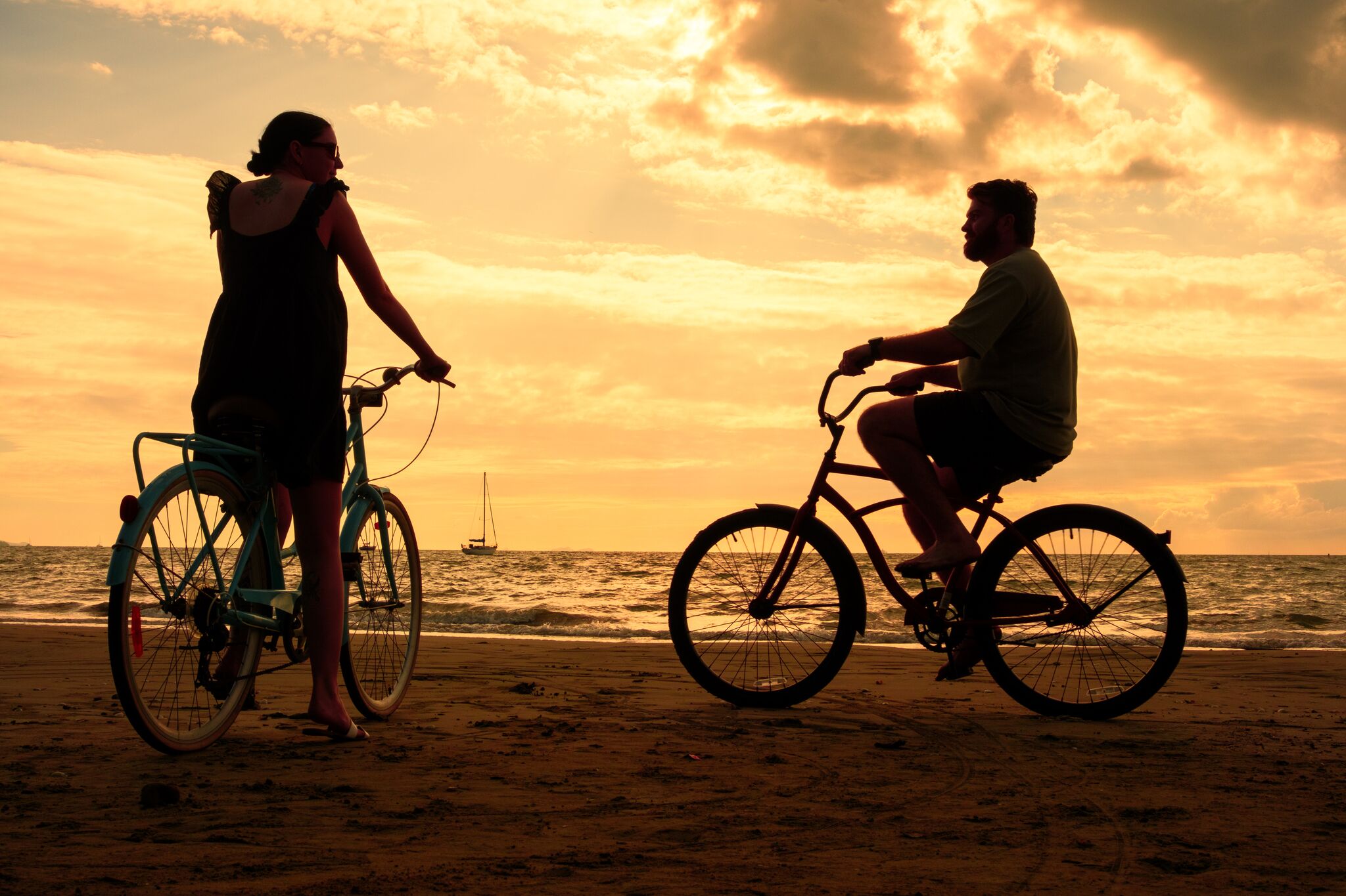 Two people on bicycles on a beach with a sunset in the background.