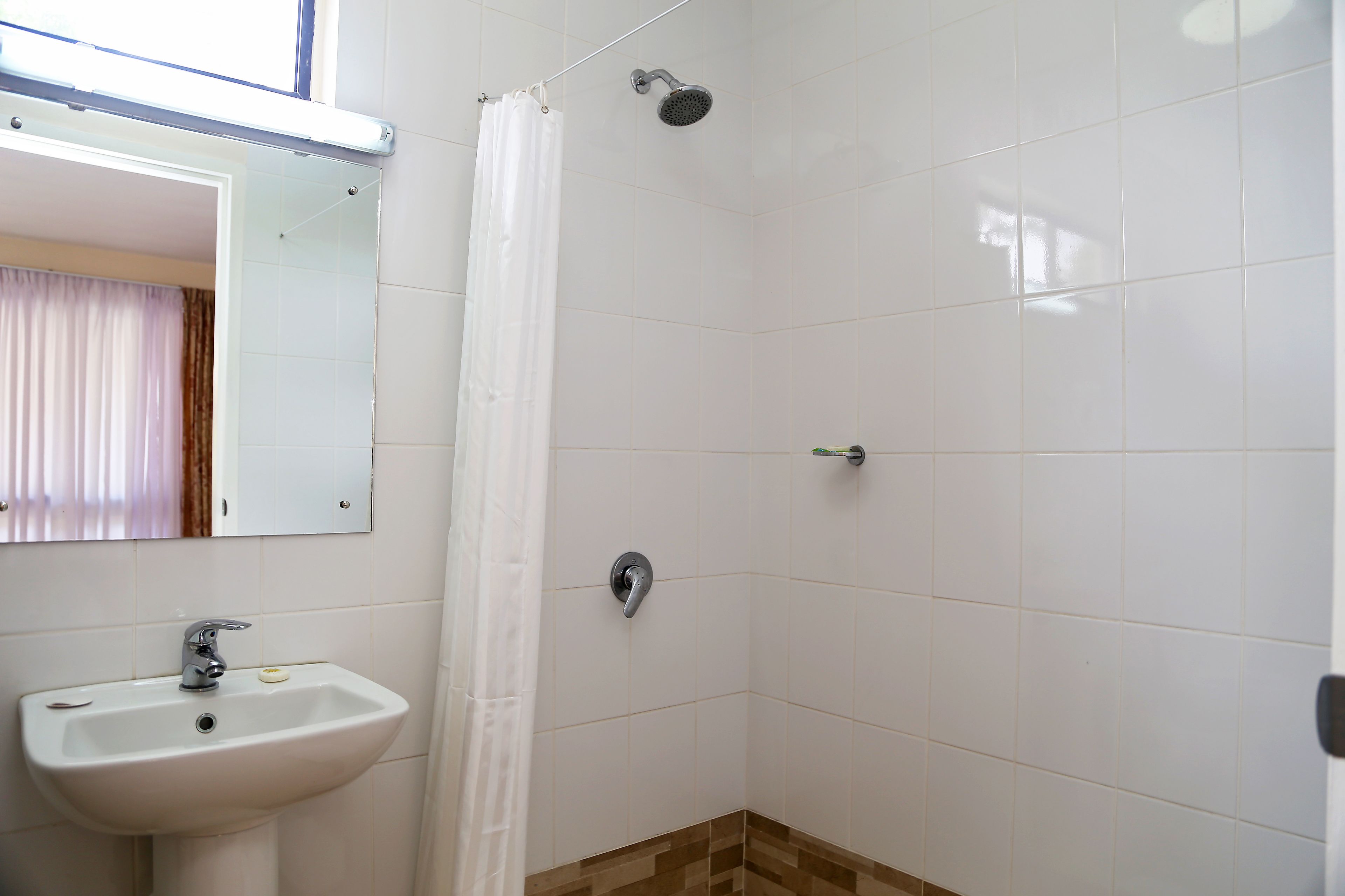 A bathroom with a white sink, a shower, and a mirror.