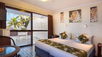 Habitación de hotel con una cama, una mesa y vistas a palmeras a través de una puerta corredera.