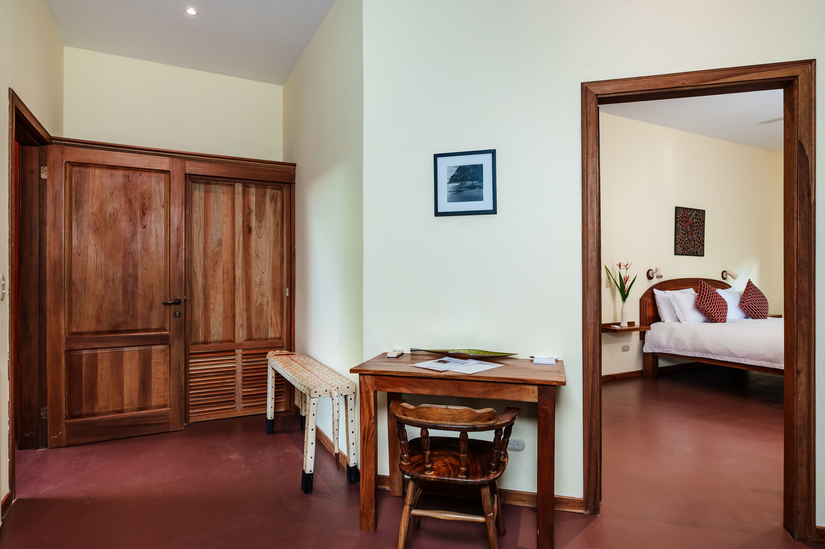 A bedroom with a bed, a wooden wardrobe, a desk with a chair, and a small table.