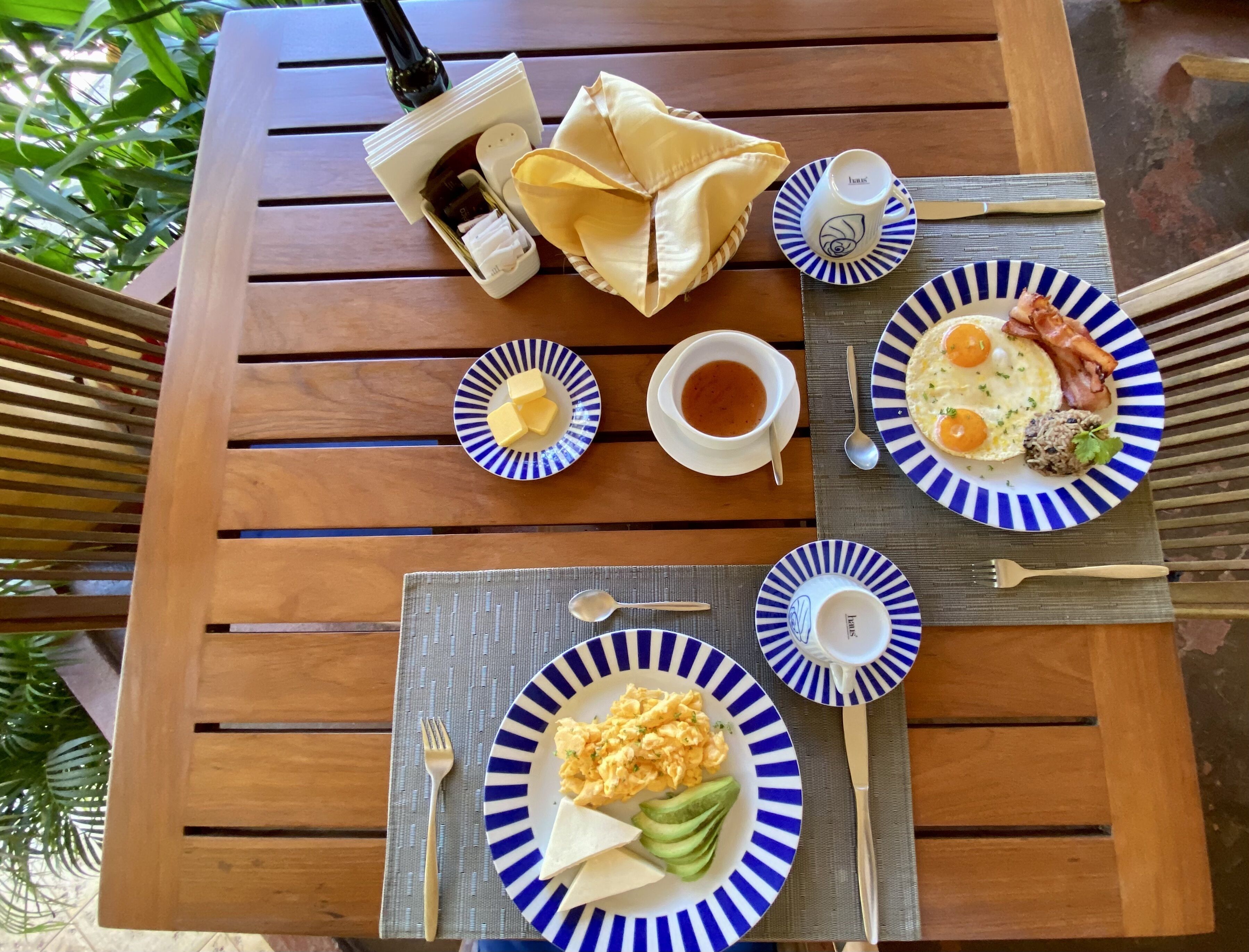 Una mesa de madera con alimentos para el desayuno, como huevos revueltos, tocino, tostadas, aguacate y mantequilla.
