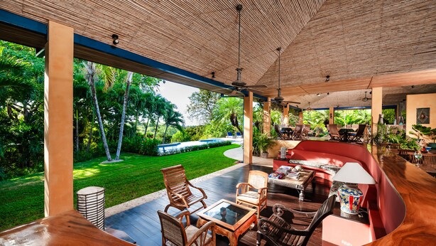 A covered outdoor seating area with wooden furniture and a view of a landscaped garden. - Hotel Luna Azul (Cuajiniquil)