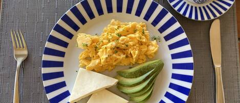 A plate with scrambled eggs, avocado slices, and cheese on a blue and white striped plate.