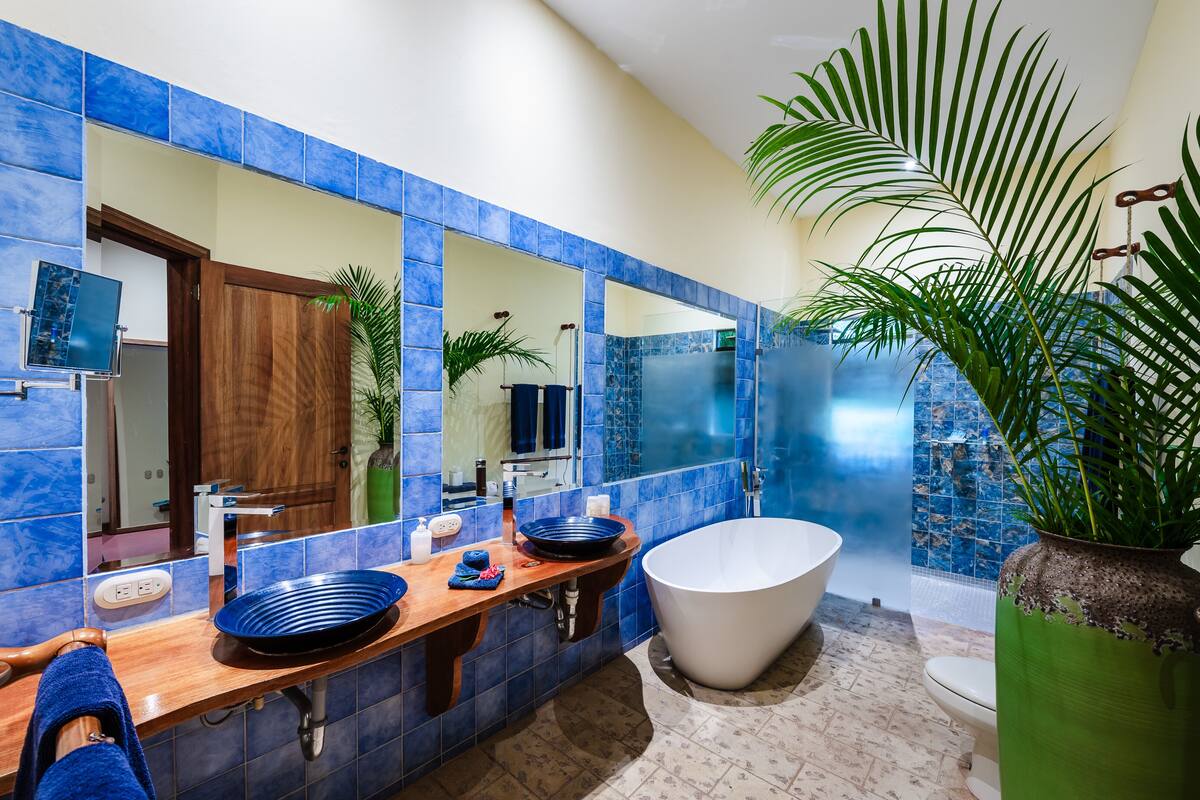 A bathroom with blue tiles, a wooden vanity, a large bathtub, and a green plant.