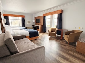 A hotel room with a bed, two armchairs, a sofa, a desk, and a TV.