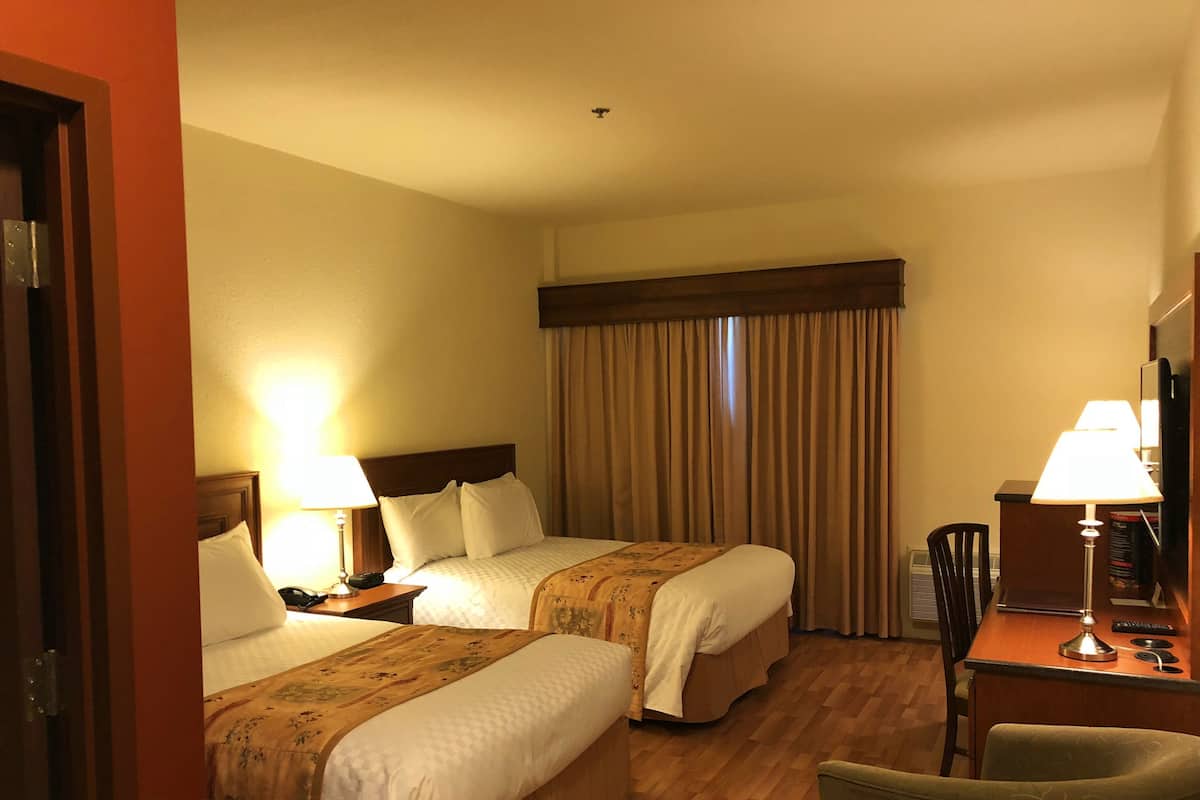 A hotel room with two beds, a desk with a lamp, a chair, and a television.