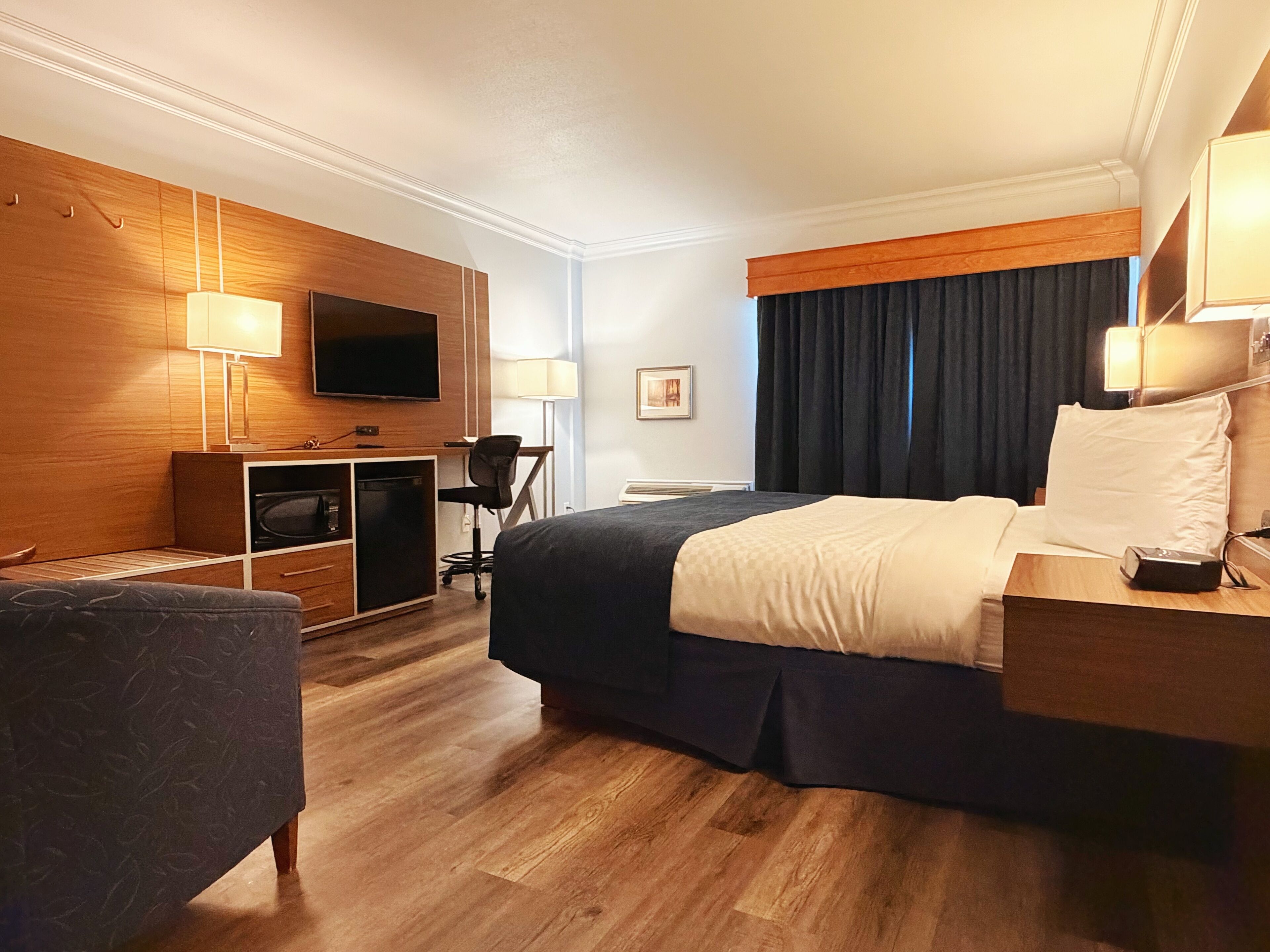 A hotel room with a bed, a desk, a television, a chair, and a desk lamp.