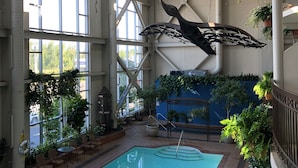 An indoor swimming pool with a large window, ceiling fans, and hanging plants.