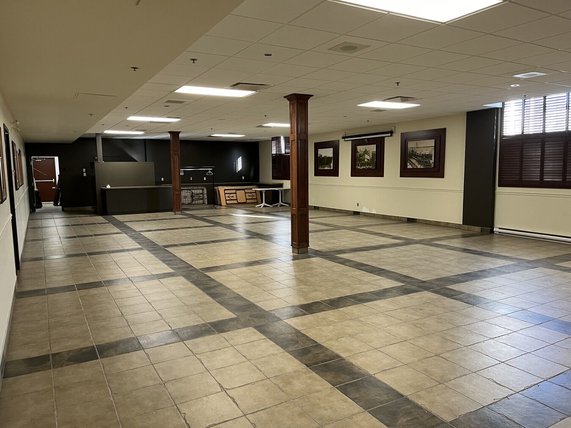 A spacious lobby with a tiled floor, a reception desk, framed pictures on the walls, and a large window with blinds.