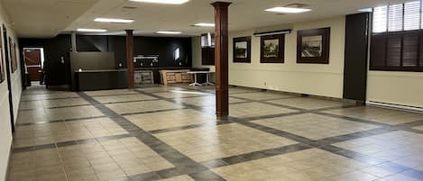 A spacious lobby with a tiled floor, a reception desk, framed pictures on the walls, and a large window with blinds.