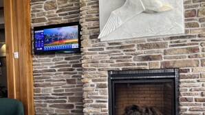 A stone wall with a fireplace, a mounted TV, and a laptop on a wooden table. - Hotel L'Oie des neiges (Levis)