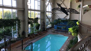 An indoor swimming pool with a large arched window, surrounded by greenery and a decorative whale sculpture.
