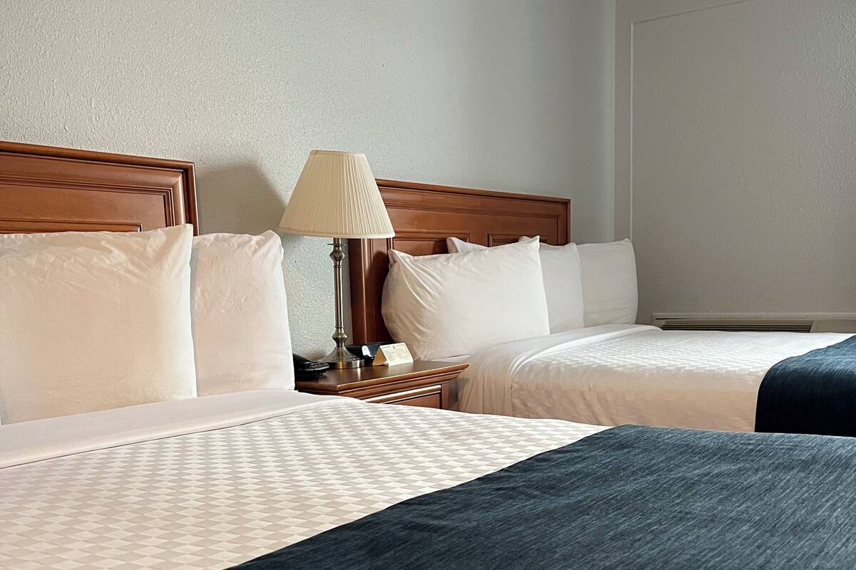 A hotel room with two beds, a nightstand with a lamp, and a wall-mounted heater.
