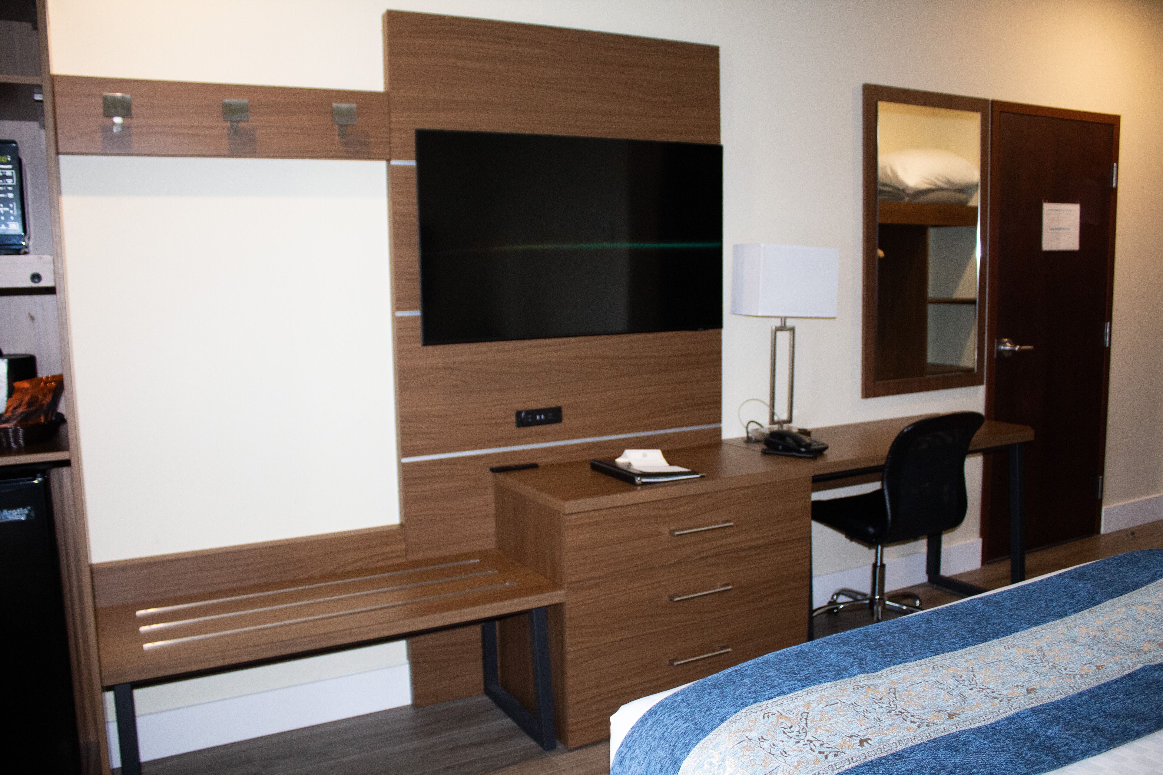 A hotel room with a bed, a desk, a chair, a TV, a wardrobe, and a bedside table.