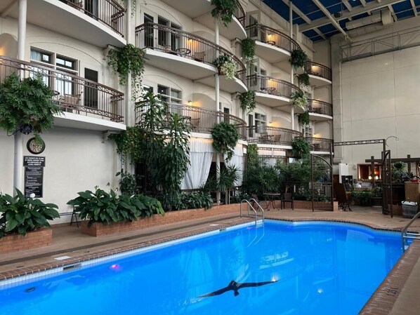 An indoor swimming pool with multiple balconies, some with plants, and a person swimming. - Hotel L'Oie des neiges (Levis)