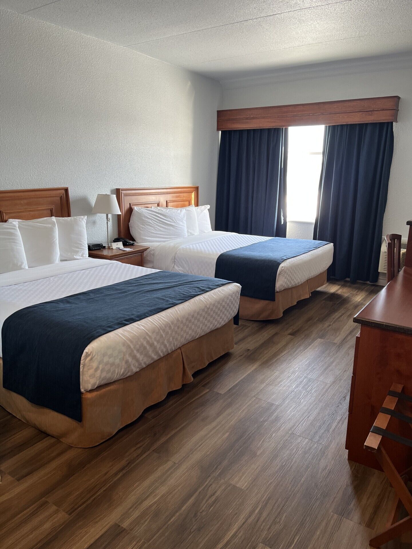 A hotel room with two beds, wooden headboards, a desk, and a window with curtains.