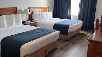 A hotel room with two beds, wooden headboards, a desk, and a window with curtains.