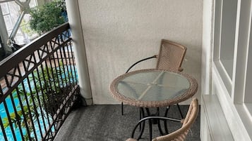 Un balcó amb taula de vidre i cadires de vimetla, una piscina al fons i una paret decorativa.