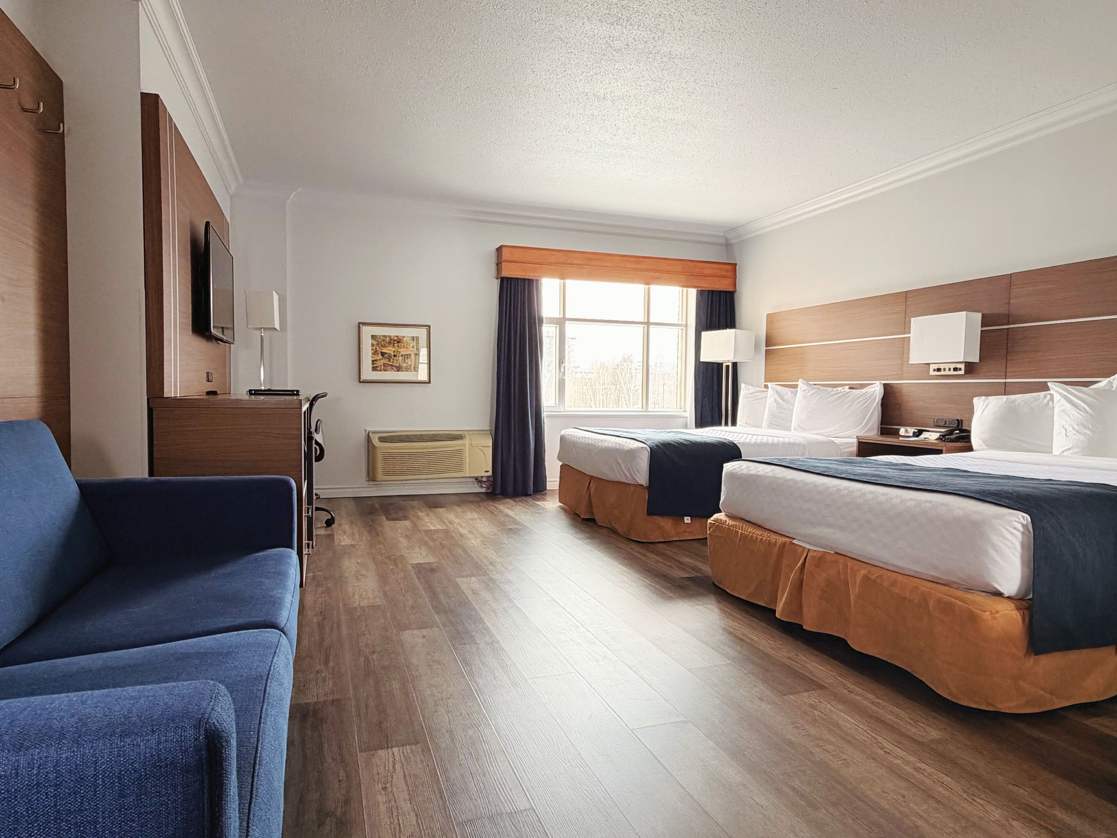A hotel room with two beds, a desk, a chair, a window with curtains, and a mounted TV.