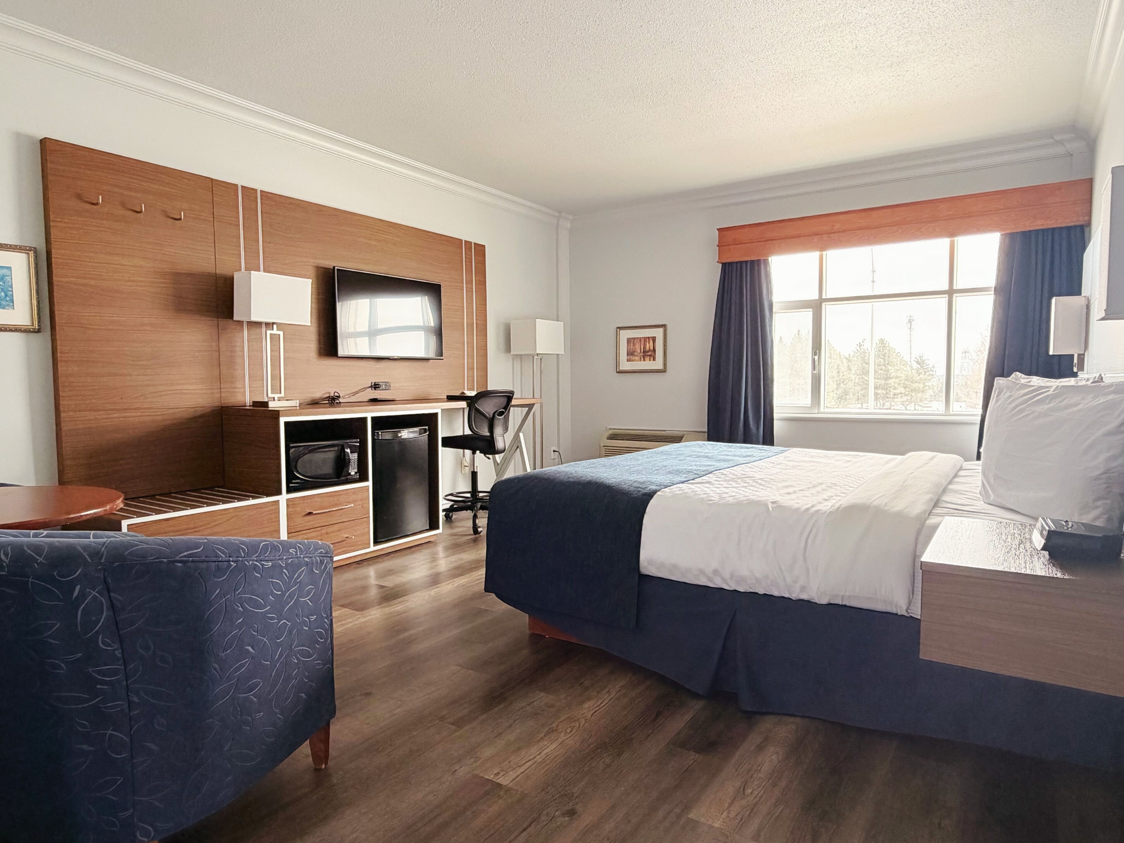 A hotel room with a bed, a desk, a chair, a TV, and a window.