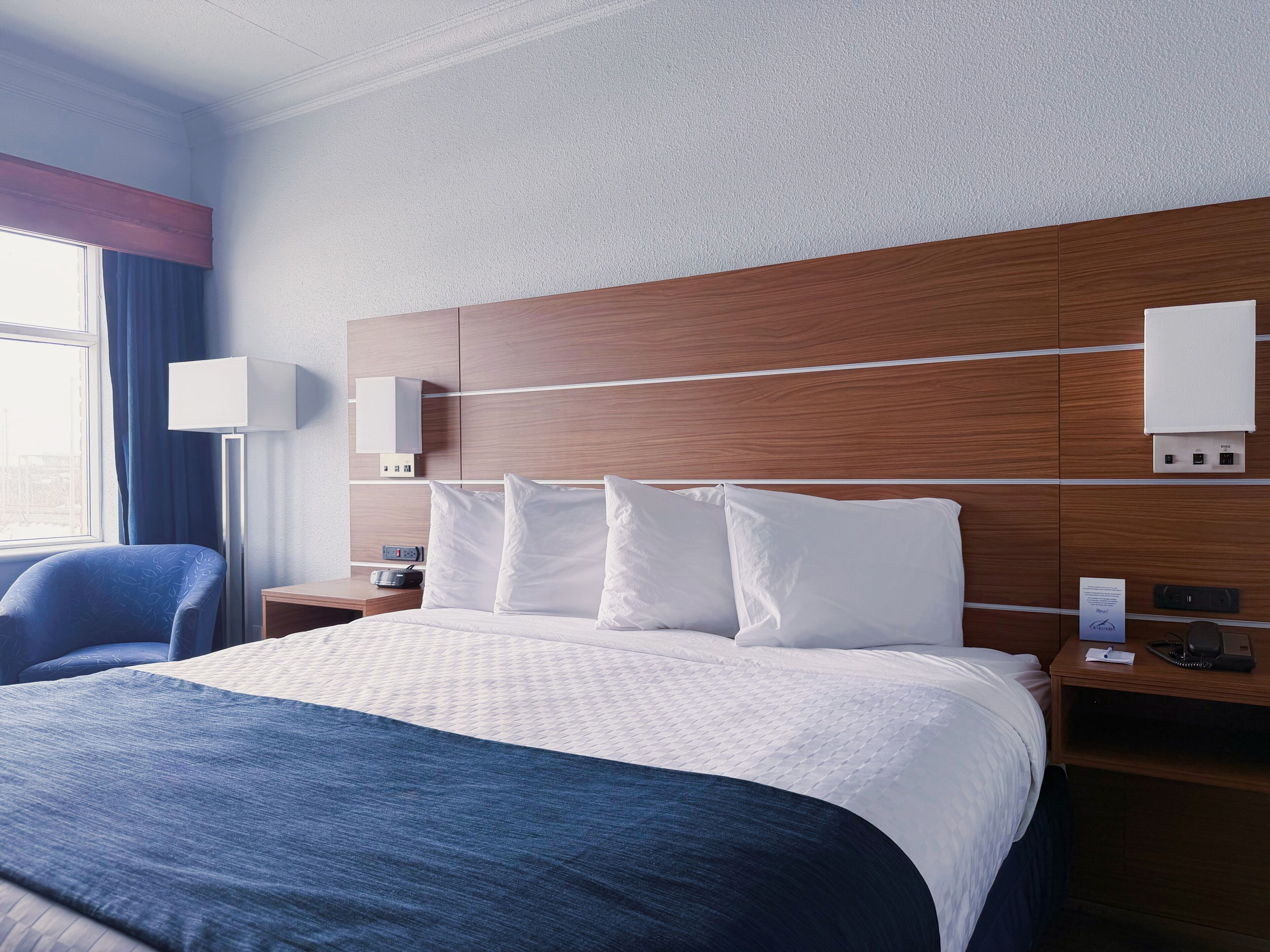 A hotel room with a large bed, a bedside table, a lamp, and a view of the city.