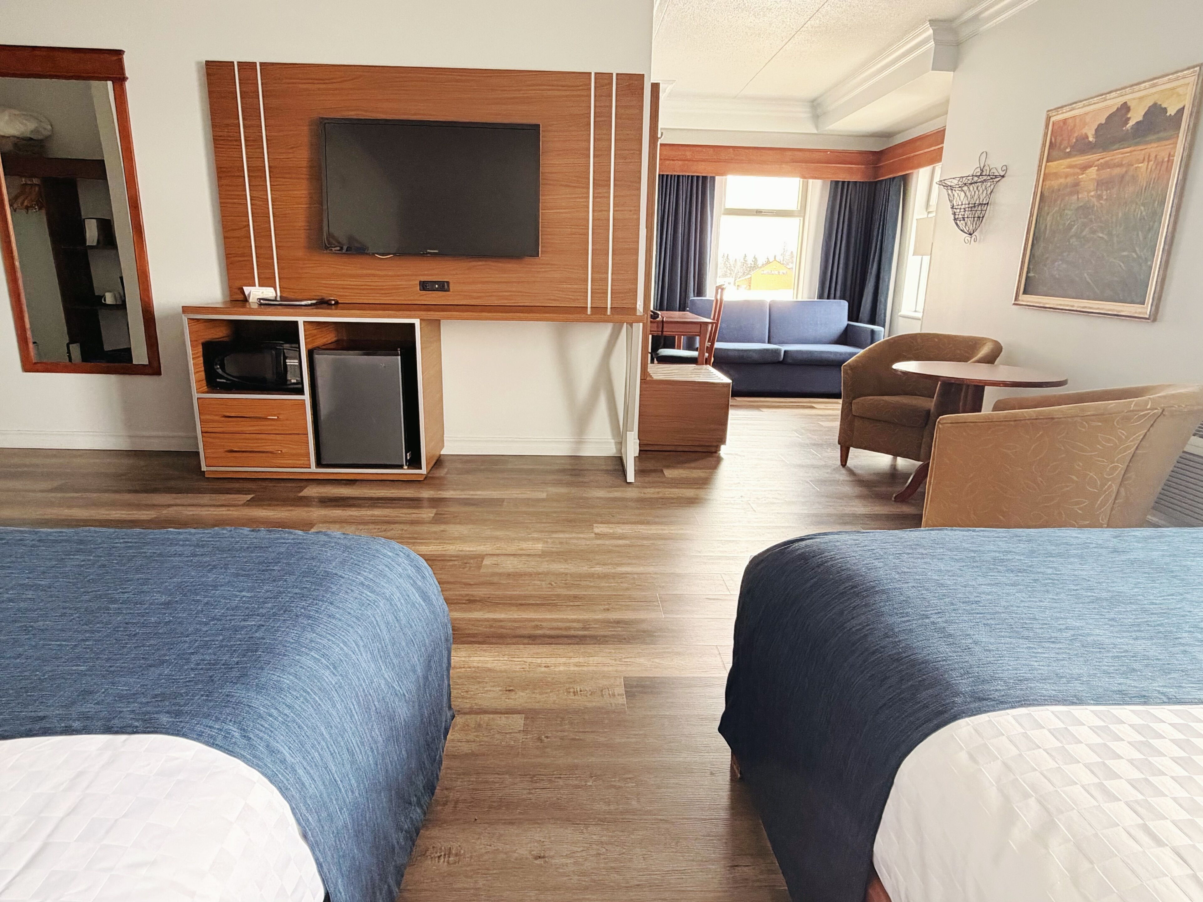 A hotel room with two beds, a TV, a small fridge, a desk, a sofa, and a chair.