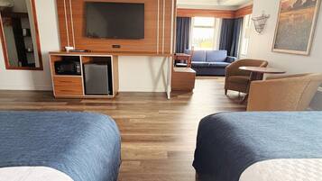 A hotel room with two beds, a TV, a small fridge, a desk, a sofa, and a chair.