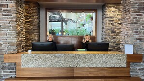A reception desk with two computers, a stone wall, and a view of indoor plants. - Hotel L'Oie des neiges (Levis)