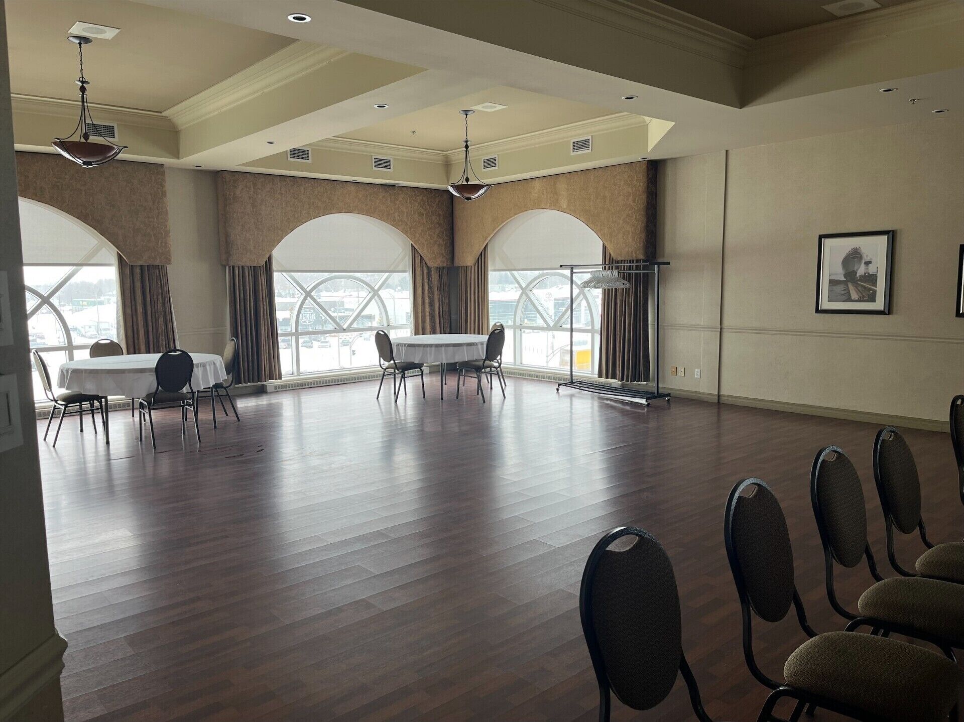 A spacious room with a high ceiling, large windows, and a table with chairs.
