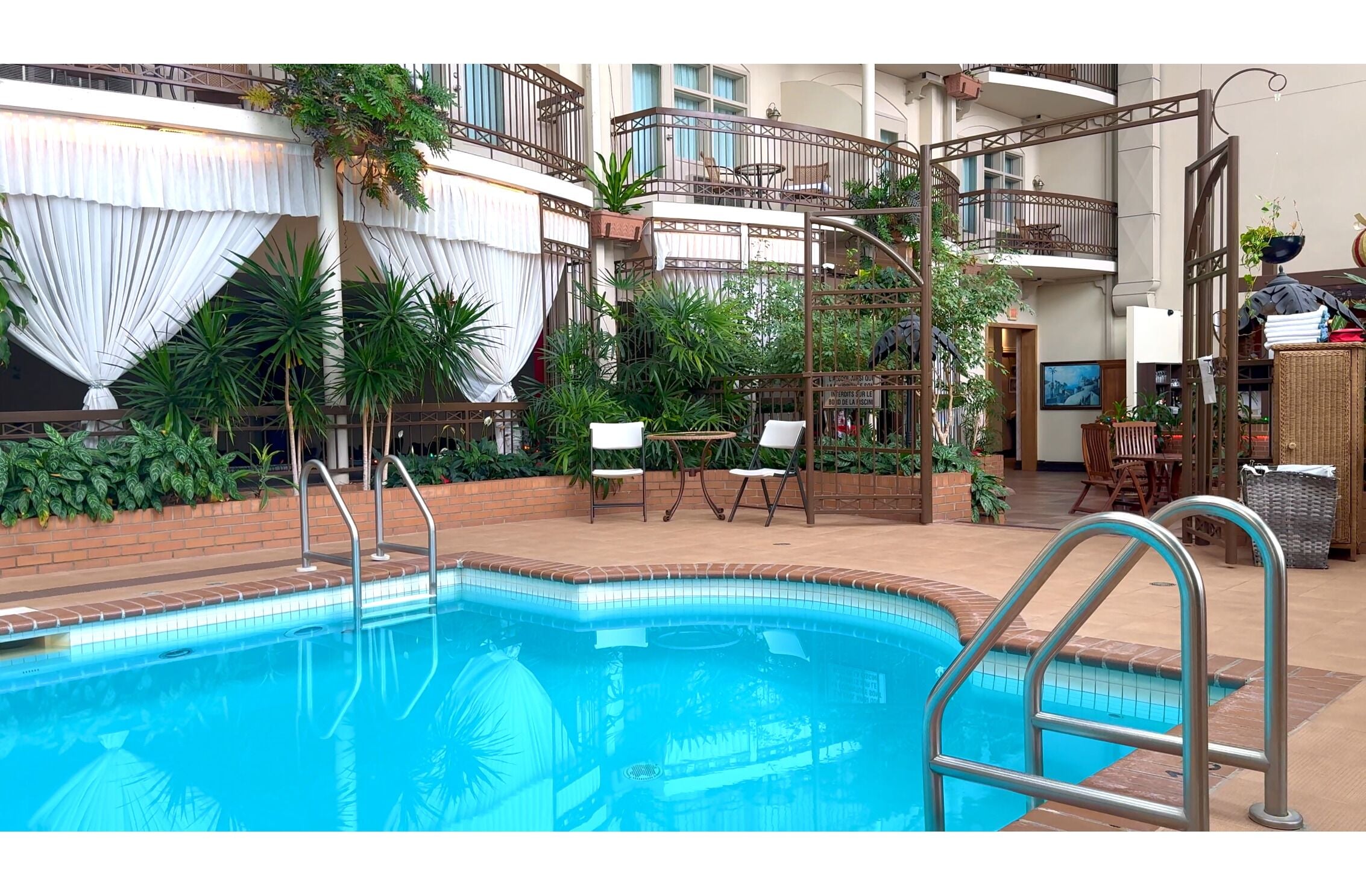 A pool area with a clear view of the pool, a set of stairs, and a seating area with chairs and tables.