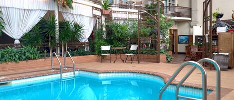 A pool area with a clear view of the pool, a set of stairs, and a seating area with chairs and tables.