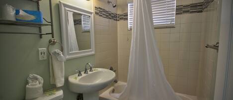 Une salle de bain avec un lavabo, des toilettes et une baignoire. On y trouve des serviettes et un rideau de douche.