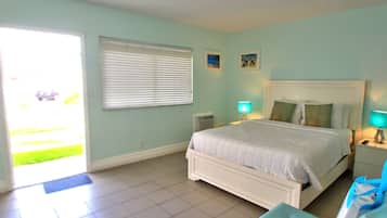 A bedroom with a bed, bedside lamps, a window with blinds, and a door leading to a balcony.