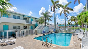 A pool area with lounge chairs, a pool ladder, and palm trees.