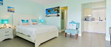 A bedroom with a bed, bedside tables, a chair, and a view into the kitchen.