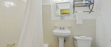 A bathroom with a bathtub, a sink, a toilet, and a shelf with toiletries.